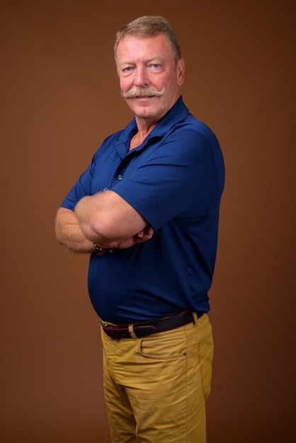 Studio shot di bell'uomo anziano con i baffi che indossa la polo blu contro il marrone