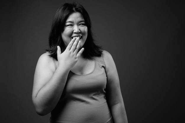 Studio shot di bella donna asiatica in sovrappeso che indossa abiti senza maniche su sfondo grigio in bianco e nero