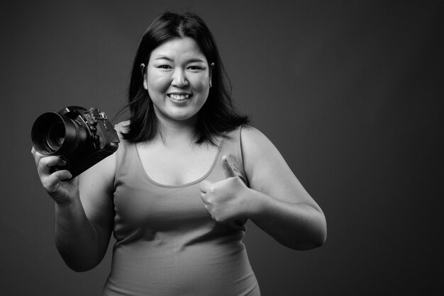 Studio shot di bella donna asiatica in sovrappeso che indossa abiti senza maniche su sfondo grigio in bianco e nero