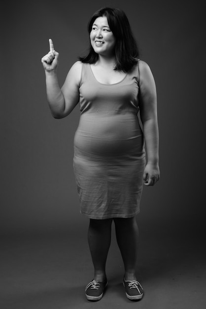 Studio shot di bella donna asiatica in sovrappeso che indossa abiti senza maniche su sfondo grigio in bianco e nero