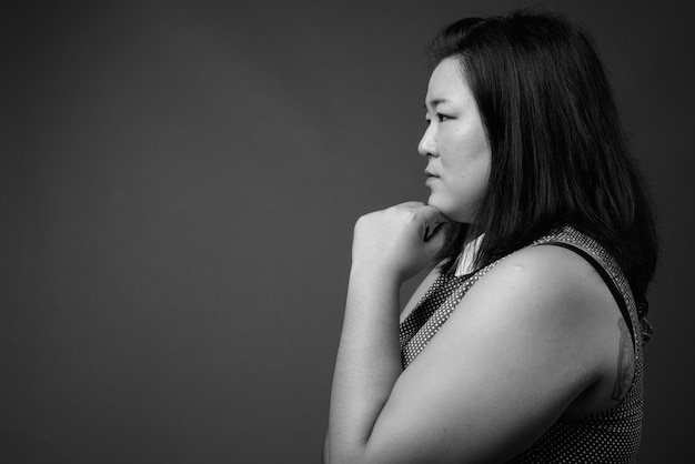 Studio shot di bella donna asiatica in sovrappeso che indossa un abito su sfondo grigio in bianco e nero