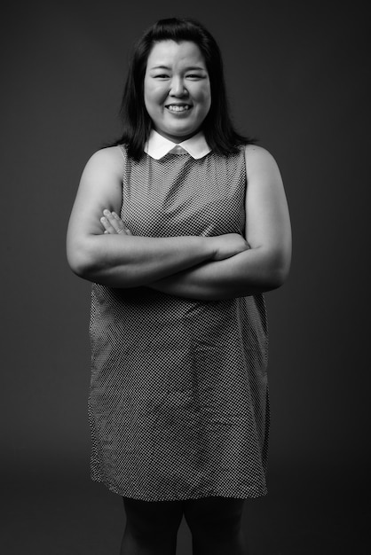 Studio shot di bella donna asiatica in sovrappeso che indossa un abito su sfondo grigio in bianco e nero