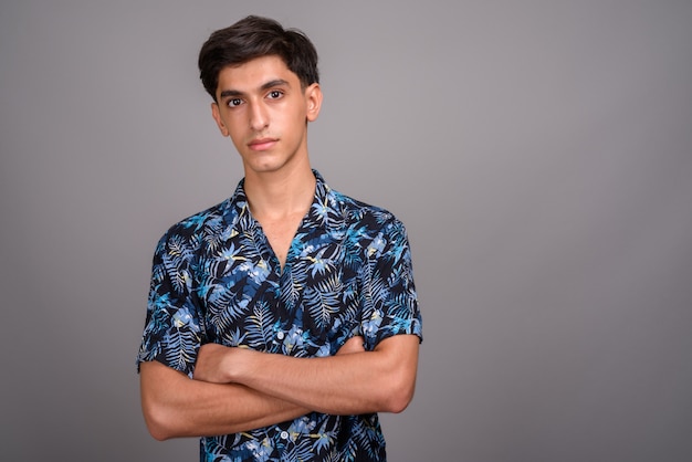 Studio shot di giovane bel ragazzo adolescente persiano che indossa camicia hawaiana su sfondo grigio