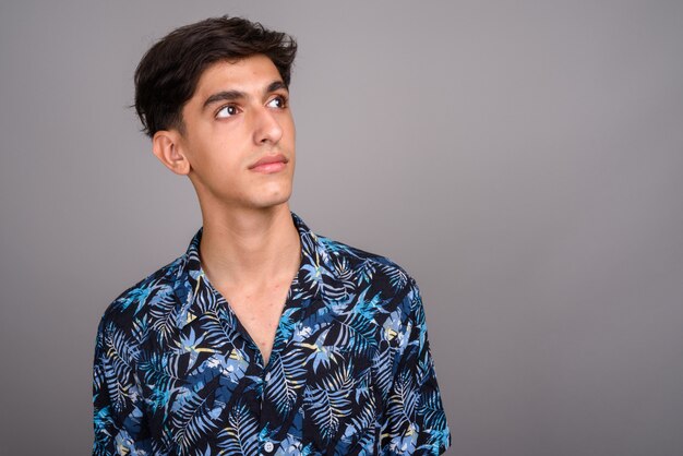 Studio shot di giovane bel ragazzo adolescente persiano che indossa camicia hawaiana su sfondo grigio