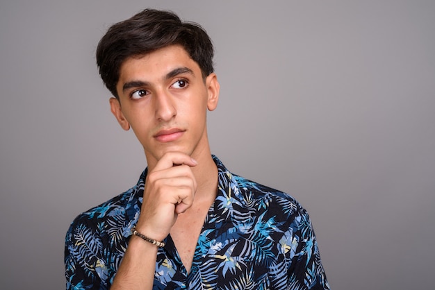 Studio shot di giovane bel ragazzo adolescente persiano che indossa camicia hawaiana su sfondo grigio