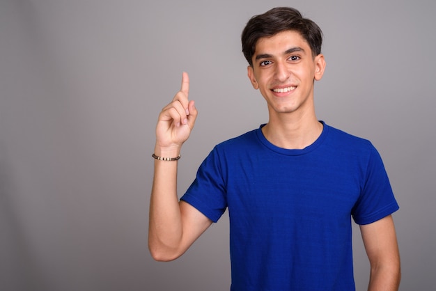 Studio shot di giovane bel ragazzo adolescente persiano su sfondo grigio