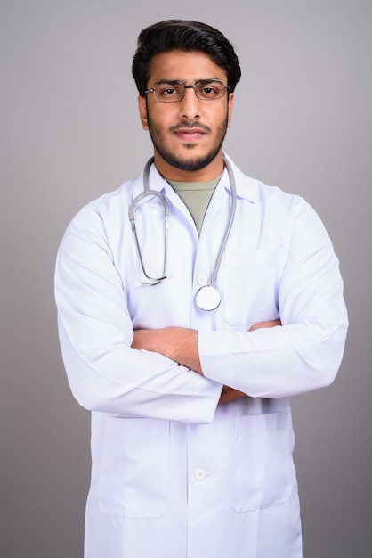 Studio shot di giovane bel uomo indiano medico contro il grigio