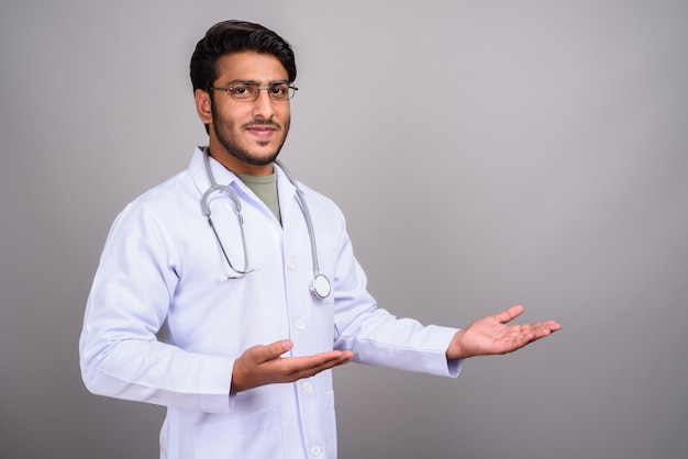 Studio shot di giovane bel uomo indiano medico contro il grigio