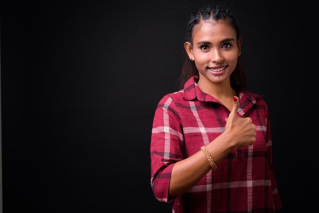 Studio shot di giovane bella donna asiatica hipster con capelli intrecciati su sfondo nero