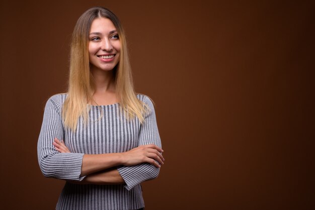 Studio shot di giovane bella donna che pensa contro il muro marrone