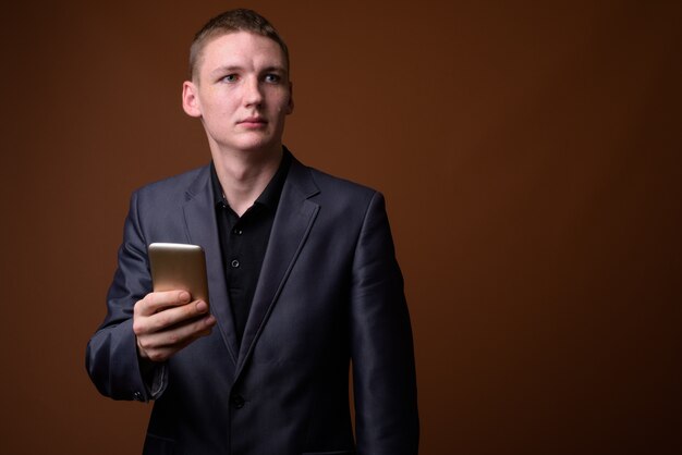 Studio shot di giovane imprenditore utilizzando il telefono cellulare su sfondo marrone