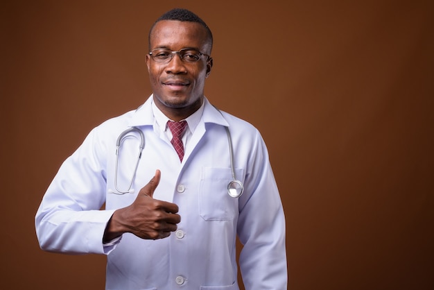 Studio shot di giovane uomo africano medico su sfondo marrone