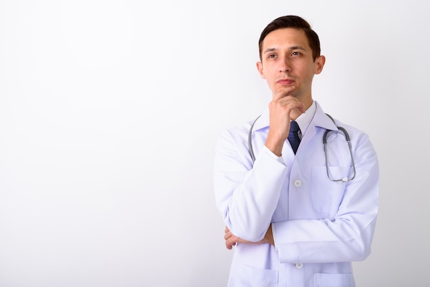 Studio shot di giovane uomo bello che pensa medico contro bianco