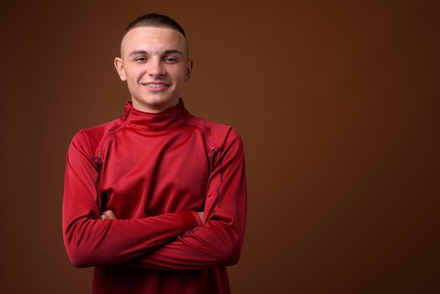 Studio shot di giovane uomo bello con i capelli corti contro il marrone