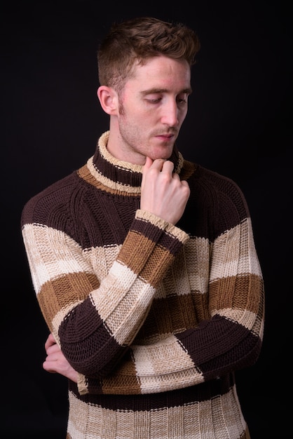 Studio shot di giovane uomo bello con maglione a collo alto pronto per l'inverno su sfondo nero