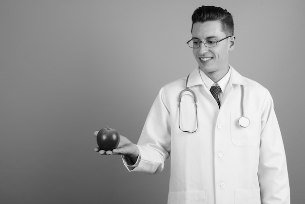 Studio shot di giovane uomo bello medico indossando occhiali da vista su sfondo grigio in bianco e nero
