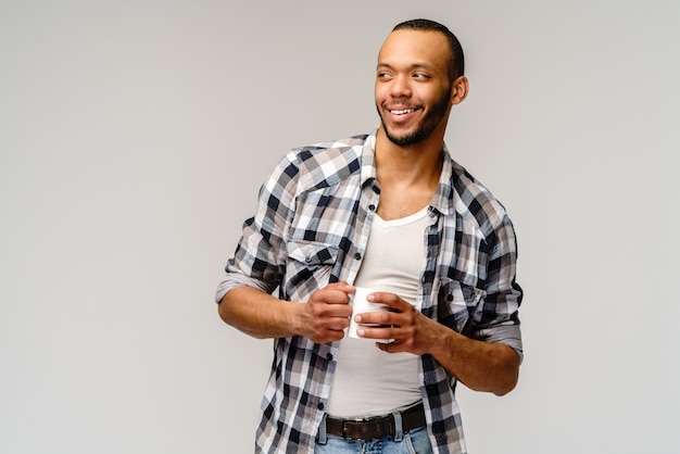 Studio shot di giovane uomo con una tazza di caffè su grigio chiaro.