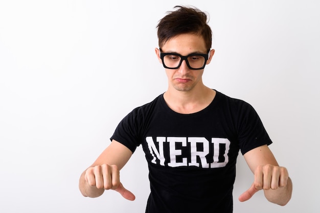 Studio shot di giovane uomo nerd che sembra triste e che dà i pollici verso il basso