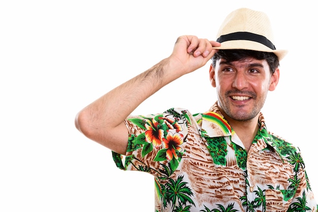 Studio shot di giovane uomo persiano felice sorridente mentre si tiene il cappello