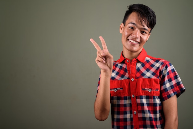 Studio shot di giovani adolescenti indiani uomo che indossa la camicia a scacchi rossa contro colorato