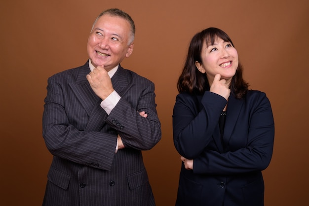 Studio shot di maturo giapponese imprenditore e maturo giapponese imprenditrice insieme su sfondo marrone
