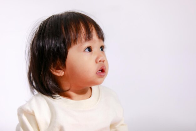 Studio shot di poco carino capelli neri corti Asian bambina figlia modello in gonna scozzese casual seduta e sorridente su sfondo bianco