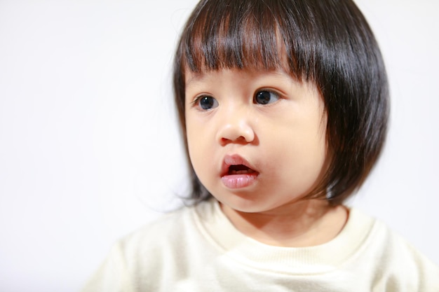 Studio shot di poco carino capelli neri corti Asian bambina figlia modello in gonna scozzese casual seduta e sorridente su sfondo bianco