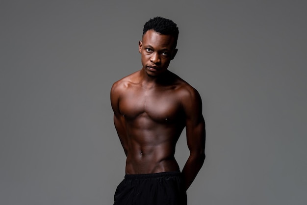 Studio shot di un bell'uomo africano in forma magra senza camicia che guarda la fotocamera su uno sfondo grigio isolato