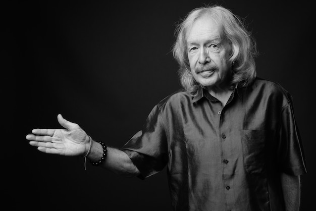 Studio shot di un uomo anziano con i baffi che indossa una camicia di seta viola contro il muro grigio