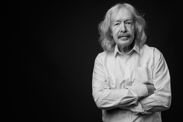 Studio shot di un uomo d'affari anziano con i baffi che indossa una maglietta rosa contro il muro grigio