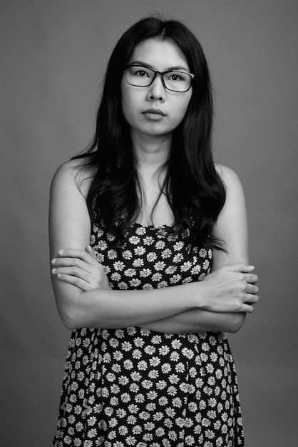 Studio shot di una donna asiatica che indossa abiti e occhiali contro uno sfondo grigio in bianco e nero