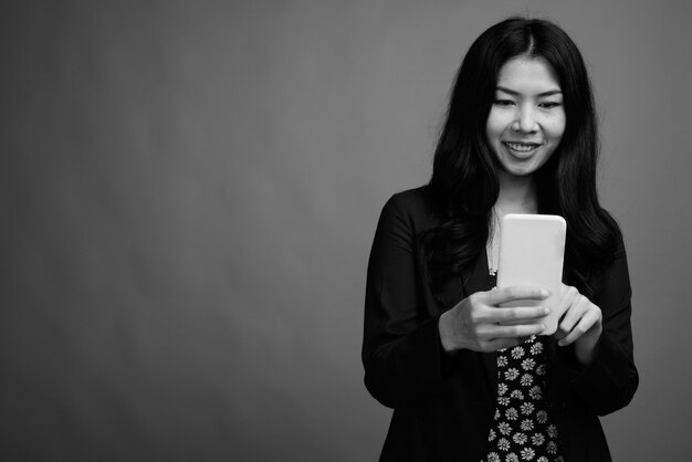 Studio shot di una donna asiatica che utilizza il telefono cellulare su uno sfondo grigio in bianco e nero