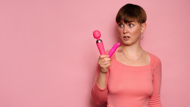 Studio shot di una giovane donna in possesso di due vibratori femminili rosa Sfondo rosa brillante Un posto per il testo o la pubblicità