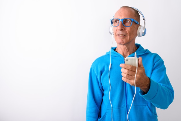 Studio shot di uomo anziano calvo tenendo il telefono cellulare mentre si pensa