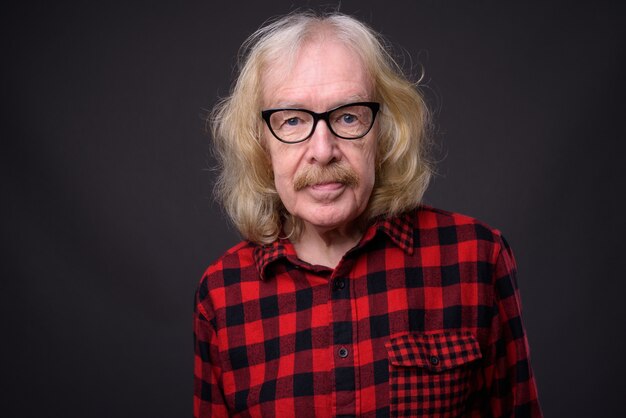 Studio shot di uomo anziano con i baffi che indossa la camicia a scacchi rossa su sfondo grigio