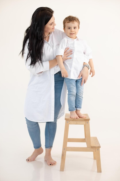 Studio verticale di mamma e figlio a piedi nudi che abbracciano e tengono il ragazzino sulla sedia di legno Bambini in rapida crescita