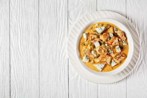 Stufato di maiale tedesco con panna, sottaceti e formaggio a muffa blu con paprika affumicata servito su un piatto bianco su fondo di legno bianco, vista dall'alto, primo piano, spazio di copia