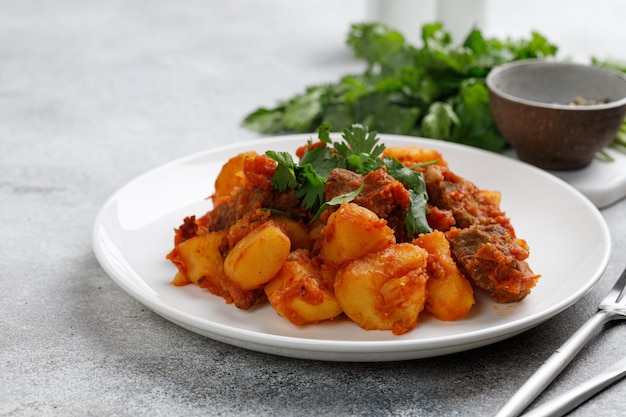 Stufato di manzo gulasch con patate Carne in umido con prezzemolo verde su piatto bianco Dinner dishxA