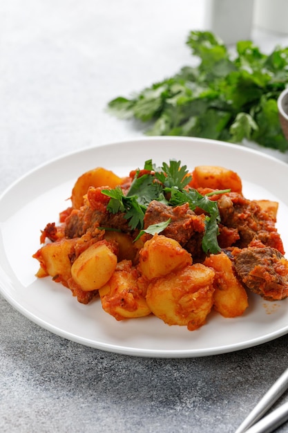 Stufato di manzo gulasch con patate Carne in umido con prezzemolo verde su piatto bianco Dinner dishxA