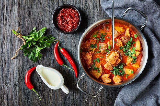 Stufato di pollo all'arrabbiata con lenticchie e patate in una pentola su un tavolo di legno, vista orizzontale dall'alto, piatto