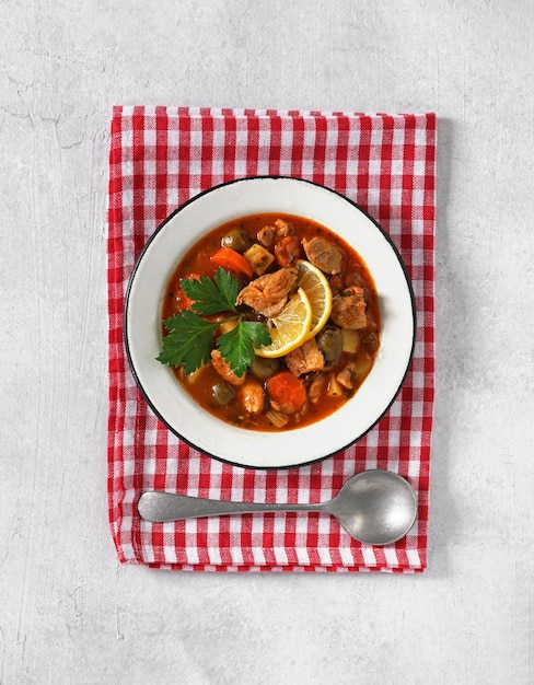 Stufato di pollo fatto in casa pollo guisado con pomodori cipolle carote olive e patate su piatto su tovagliolo rosso copia spazio vista dall'alto