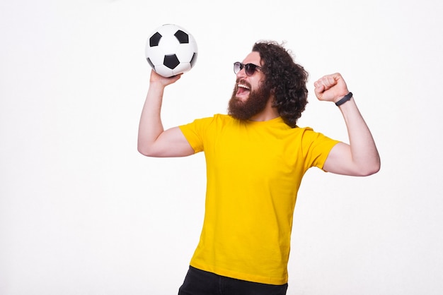 stupito hipster barbuto con capelli ricci lunghi che tiene il pallone da calcio e celebra il successo