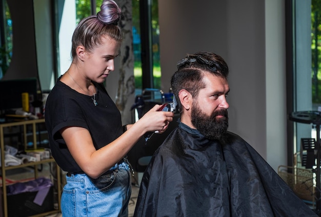 styling di capelli e barba. il ragazzo brutale con il maestro professionista del barbiere usa il rasoio elettrico. Cura personale. cura del barbiere maschio. uomo barbuto alla poltrona del parrucchiere nel salone. bellezza e moda.