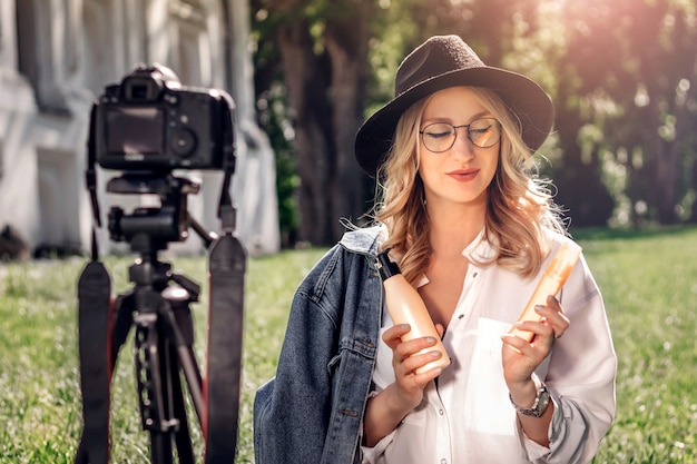 Stylish girl blogger sitting on the street on the grass and shoots vlog on camera. 
