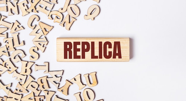 Su fondo chiaro, lettere in legno e un blocco di legno con la scritta REPLICA. Lay piatto