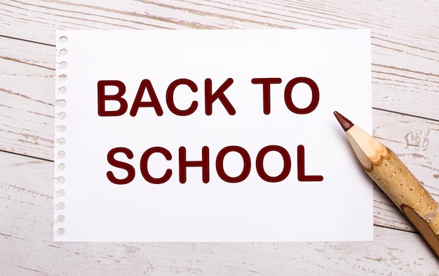Su fondo di legno chiaro una matita colorata e un foglio bianco con la scritta BACK TO SCHOOL