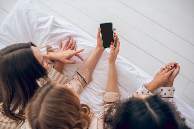 Su internet. Ragazze con smartphone sdraiato sul letto e guardare qualcosa