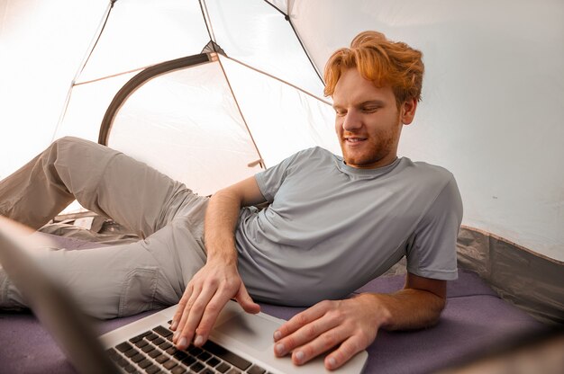 Su internet. Un giovane sdraiato in una tenda con un laptop