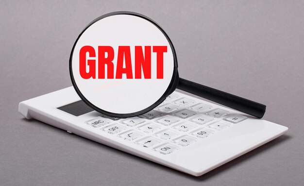 Su sfondo grigio calcolatrice nera e lente di ingrandimento con testo GRANT.Business concept