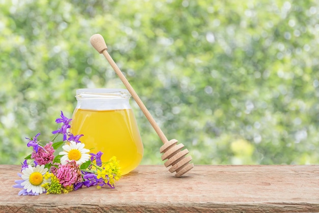 su sfondo sfocato, un vasetto di miele fresco e un bouquet di fiori di campo